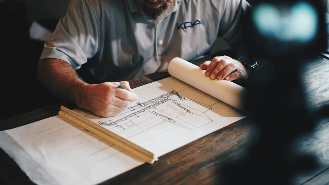 Hand drawing a building plan on rolled drawings at a desk